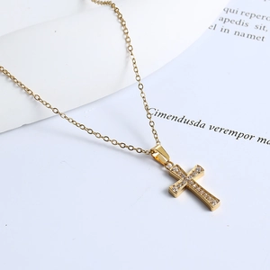 Detailed view of a gold cross pendant necklace featuring cubic zirconia on a white surface