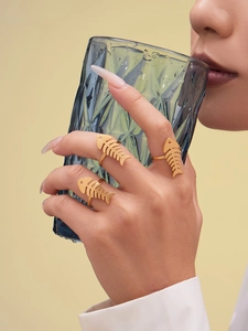 Detailed view of three gold-plated herringbone rings on a hand holding a blue glass