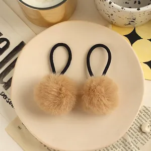 Close-up of fluffy khaki faux fur pom pom hair ties displayed on a ceramic dish
