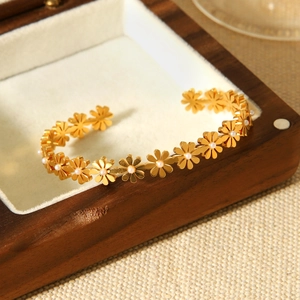 Detail of 18K gold stainless steel open bangle featuring daisy charms and white pearls