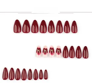 Faux ongles amande rouge foncé avec motifs de cœur et détails de perles dorées