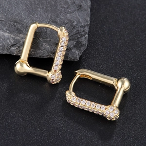 Geometric gold hoop earrings with sparkling white zircon stones on dark stone background