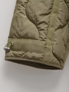 Detailed view of army green quilted jacket with wavy stitching and adjustable metal toggle