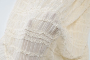 Détail du tissu plissé blanc cassé montrant la texture translucide et les volants