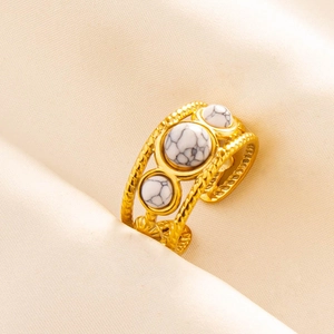 Macro detail of gold braided open ring featuring three white marble stones on satin fabric
