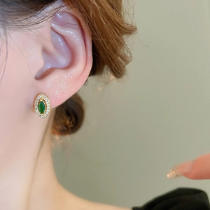 Close-up of vintage gold stud earring with marquise green zircon and white crystal border