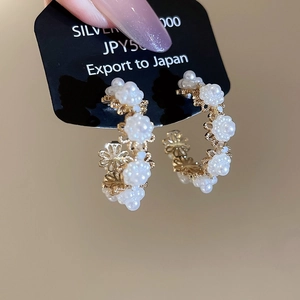 Detail of gold floral hoop earrings featuring white pearl clusters and intricate cutouts