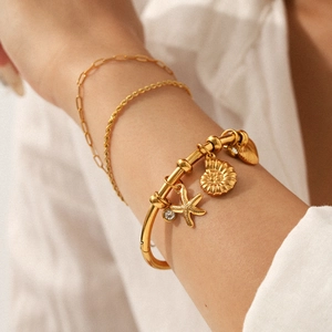 Close-up detail of 18K gold plated stainless steel bracelet with starfish and shell charms