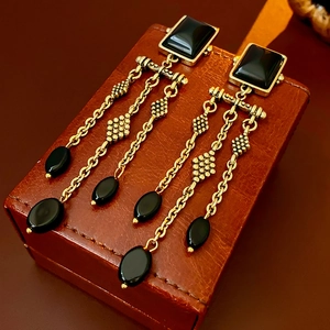 Macro shot of vintage gold tassel earrings with black stones on a leather surface