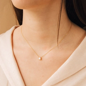 Detail of a pear-cut zircon pendant on a gold chain necklace worn by a model