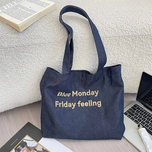Dettaglio della borsa tote in denim blu con ricamo giallo su sfondo di pavimento chiaro