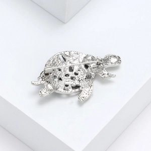 Silver turtle brooch back view showing secure pin and textured metal craft on white stand