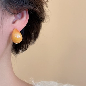 Close-up of translucent amber orange resin teardrop stud earrings on female ear