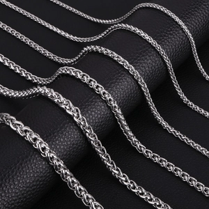 Macro shot of silver stainless steel wheat and rope chains on black leather surface
