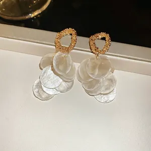 Elegant gold round earrings with white iridescent shell tassels on a cream leather base