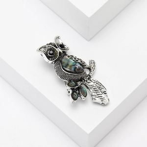 Vintage silver owl brooch with iridescent abalone shell inlay on a white pedestal