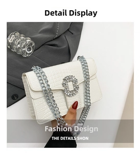 Close-up of white crocodile pattern bag featuring a rhinestone buckle and silver chain