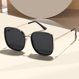 Fashionable oversized black sunglasses with gold metal temples on a minimalist background