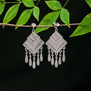 Detail of silver geometric hollow earrings with leaf tassels on a dark background