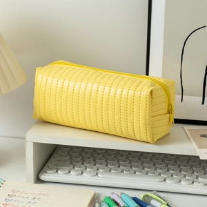 Close-up of bright yellow quilted PU leather pencil case with metal zipper on a desk