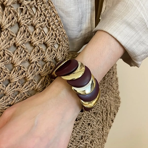 Macro detail of wine red and gold layered chunky stretch bracelet worn on wrist