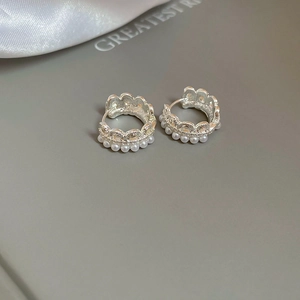 Macro detail of silver crown lace earrings featuring white pearls and elegant silk background