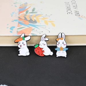 Close-up of three cute white rabbit enamel pins with carrot, strawberry and flower bow details