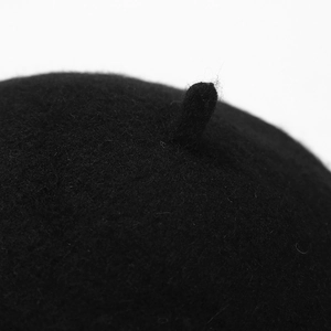 Detailed close-up of a black wool beret top featuring the classic stem and felt texture