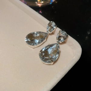 Detail shot of silver teardrop crystal earrings on a beige velvet display tray