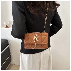 Close-up of brown quilted shoulder bag featuring gold chain strap and tassel detail