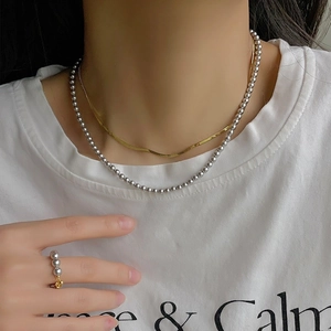 Detail of layered gold snake chain and silver bead necklace with matching bead ring