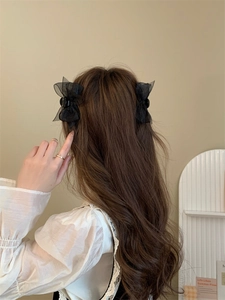 Pair of black mesh bow hair clips worn on wavy hair shown from a back view perspective