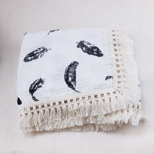 Detail of baby muslin swaddle featuring black feather prints and delicate tassel edges