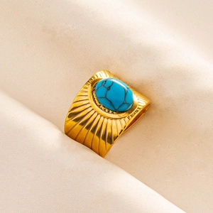 Close-up of a wide gold ring featuring radial sunburst texture and an oval turquoise stone