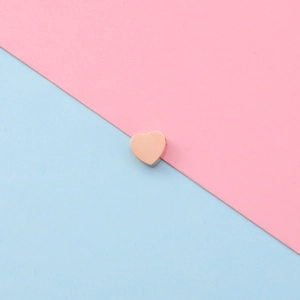 Close-up of polished rose gold heart-shaped charm on pink and blue background
