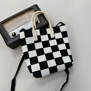Detail view of a black and white checkerboard knit bag with ivory handles and vintage radio