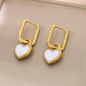 Vue macro des boucles d'oreilles rectangles dorées avec breloque cœur blanc texturé