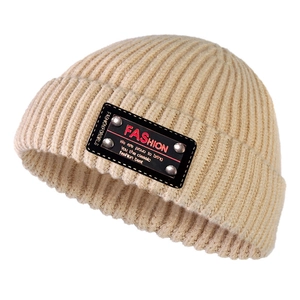 Dettaglio del berretto in maglia beige con trama a costine e patch con rivetti