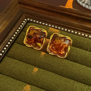 Detailed shot of amber resin square earrings in twisted gold metal on green velvet