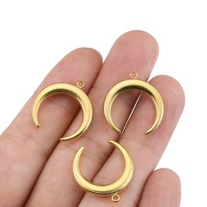 Golden crescent moon pendants in stainless steel held by hand for scale and detail