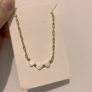Detail of gold necklace with three white heart pendants on display card