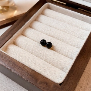 Close-up of minimalist black round stud earrings in a vintage wooden jewelry box