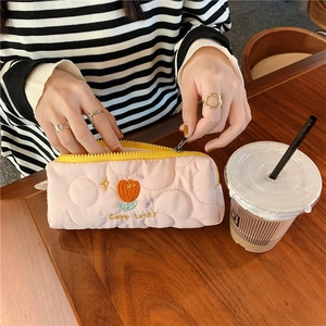 Quilted pink tulip pencil case with Good Luck embroidery held over a wooden table