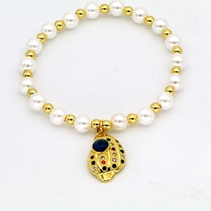 Makroansicht des Perlenarmbands mit goldenem Muschel-Anhänger und blauem bösem Blick