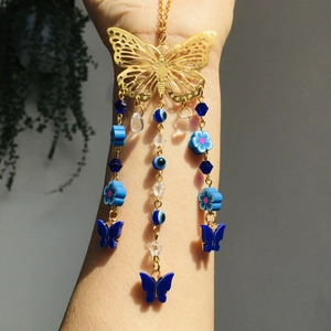 Detailed shot of golden butterfly car charm with blue evil eye beads on a model's arm