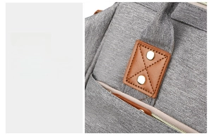 Detail of grey fabric diaper bag with reinforced brown leather patch and metal rivets