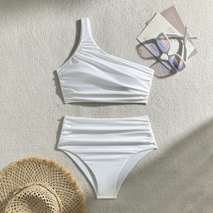 Flat lay of white one-shoulder bikini set with ruched texture on beige rug background
