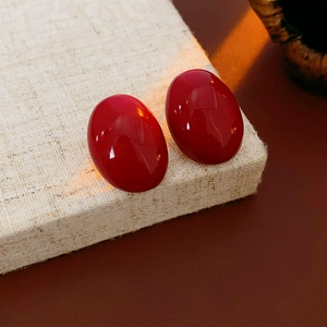 Macro detail of red oval enamel earrings on light linen texture with warm lighting