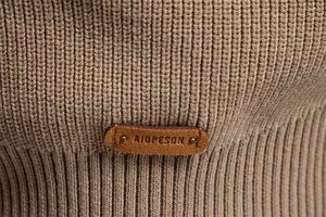 Close-up of warm khaki ribbed knit texture and premium brown leather logo tag