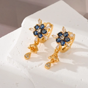 Detail of flower-shaped copper earrings with blue and white zircon stones on stone texture